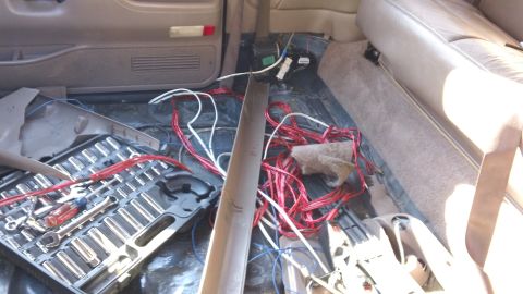 1994 Ford Bronco - Interior mid-teardown with the front carpet pulled up to expose the dark painted floor pan, coils of red and white speaker wire, and a remo…