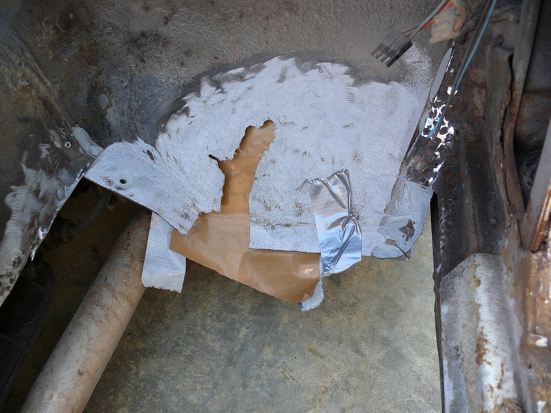 Underbody repair with white filler, brown paper, and silver tape on a concrete floor