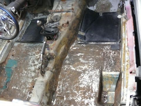 1976 Chevrolet Corvette - The interior floor of a car shows significant rust and damage, with a manual shifter visible.