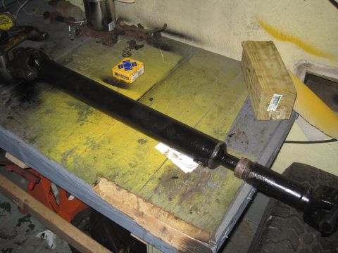 1979 Ford Bronco - A black driveshaft rests on a cluttered workbench, suggesting a repair or maintenance activity.