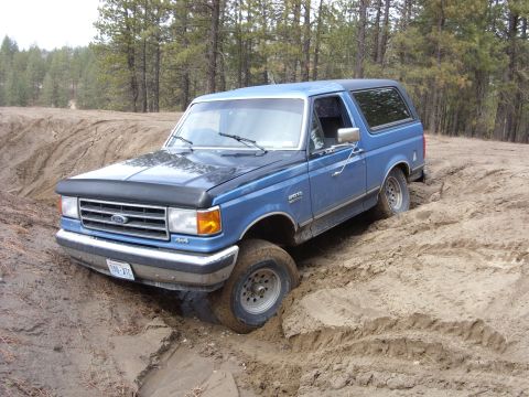1988 Ford Bronco - This 1988 Ford Bronco is shown off-roading on a dirt track, with its front right wheel stuck in the mud.