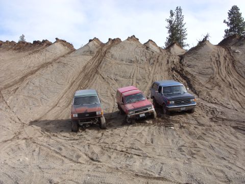 1988 Ford Bronco - Three SUVs navigate a challenging sandy terrain with tire tracks marking the slopes.