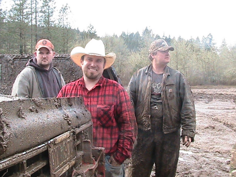 three men standing in mud, one wearing a cowboy hat