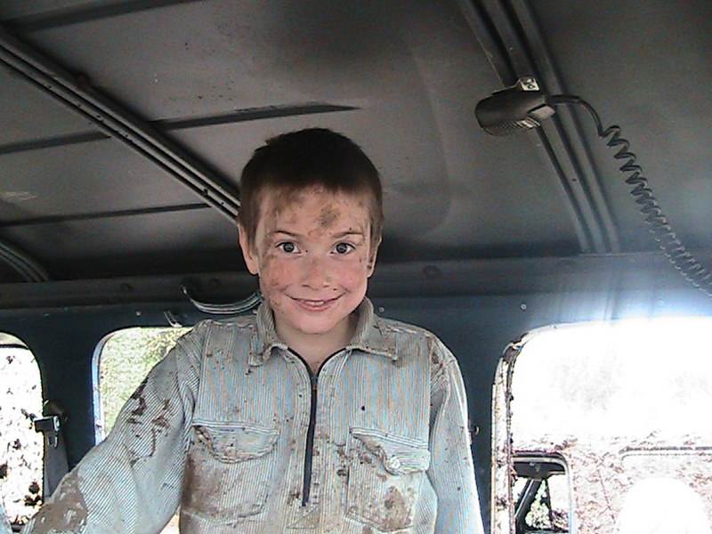 Child with dirt on face and clothes smiles inside a vehicle