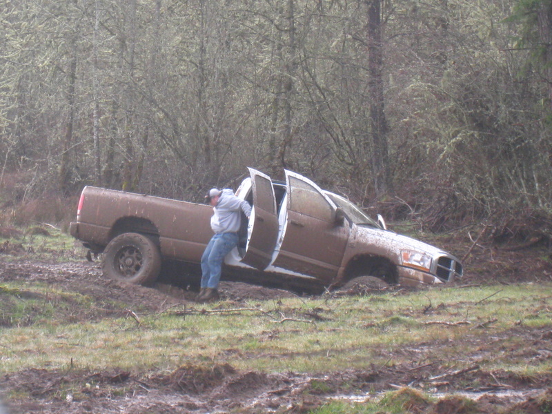 guy getting out of a brown pickup truck stuck in the mud with doors open