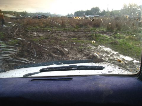 1978 Ford Bronco - A muddy field with multiple vehicles visible in the distance, seen from the perspective of someone inside a vehicle.