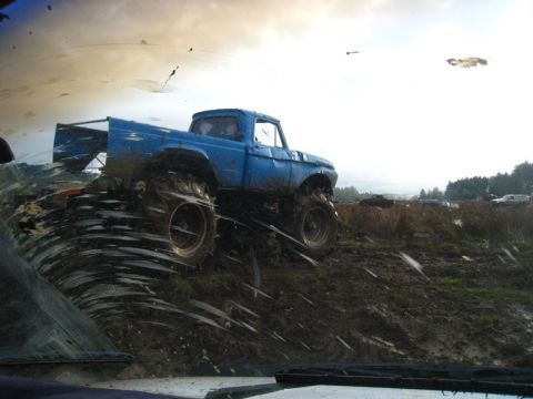 1978 Ford Bronco - A blue pickup truck navigates a muddy terrain, kicking up dirt and water as it goes.