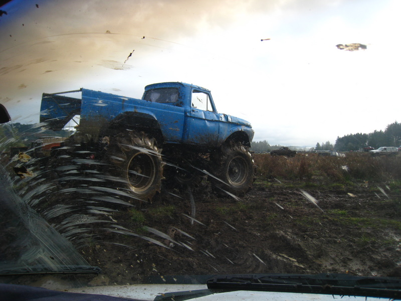 Blue pickup truck with large tires driving through mud
