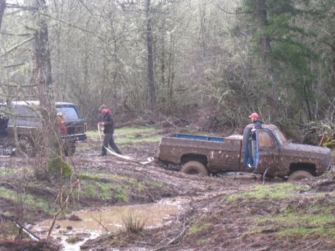 1978 Ford Bronco - Two trucks are stuck in the mud in a wooded area, with people attempting to free them.