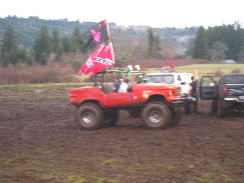 1978 Ford Bronco - A red off-road vehicle navigates a muddy terrain, accompanied by other vehicles and a distinctive flag.