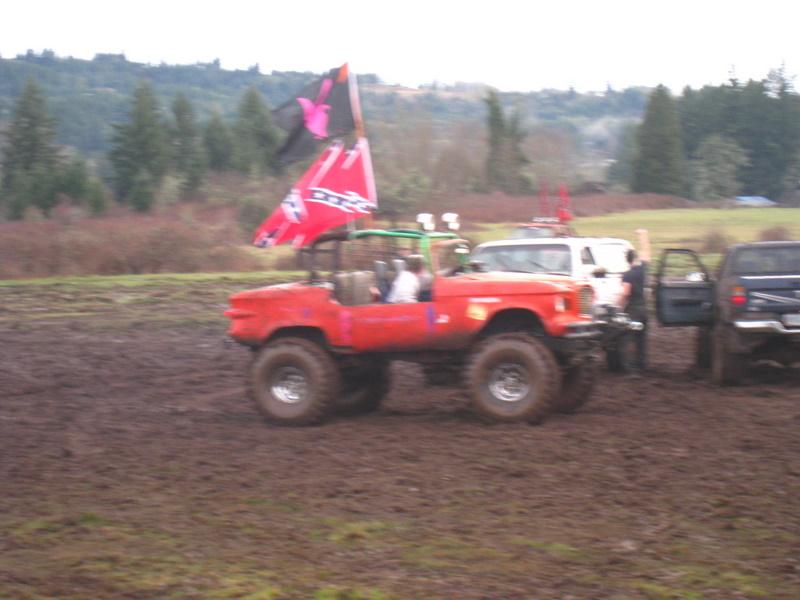 Red off-road vehicle with large tires and a flag flying in a muddy field