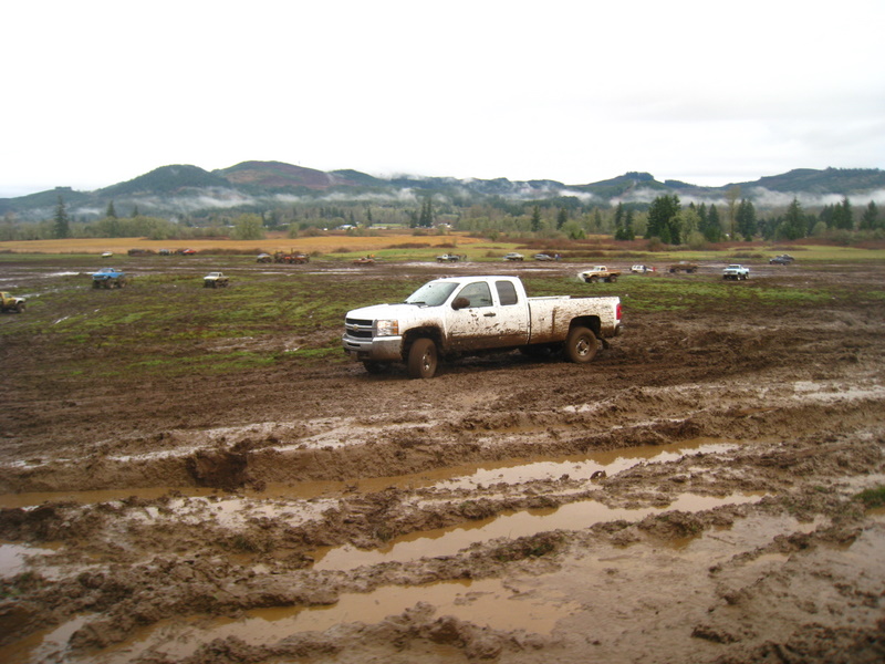 White pickup truck in a muddy field with other vehicles in the background