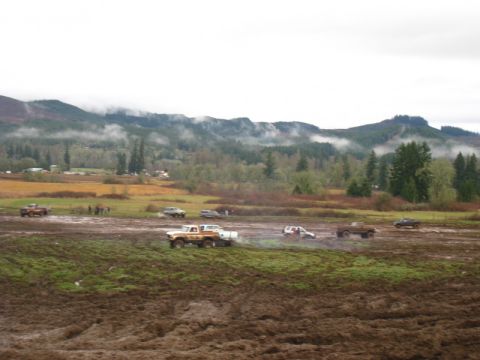1978 Ford Bronco - Multiple vehicles navigate a challenging muddy terrain under a cloudy sky, with forested hills in the distance.
