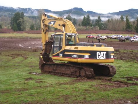 1978 Ford Bronco - An excavator sits in a muddy field, with other vehicles visible in the distance.