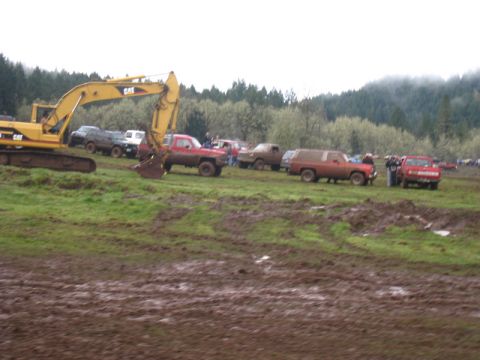 1978 Ford Bronco - An excavator sits in a muddy field alongside several trucks, suggesting an off-road event or construction site.