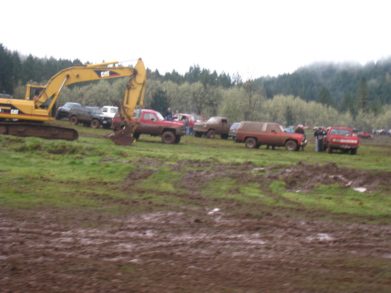 Muddy field with excavator and multiple trucks parked in the background