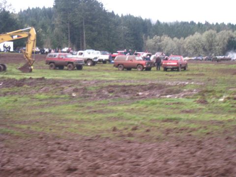 1978 Ford Bronco - Off-road vehicles and an excavator are gathered in a muddy field with trees in the background.