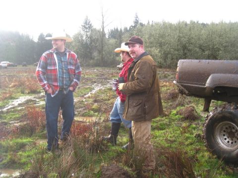 1978 Ford Bronco - Three men stand in a muddy field next to a dirty pickup truck, with other vehicles visible in the background.