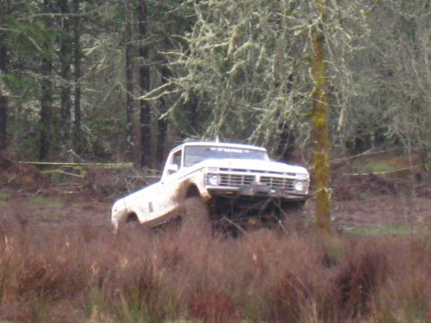 1978 Ford Bronco - A white pickup truck navigates a muddy terrain, kicking up dirt as it goes.