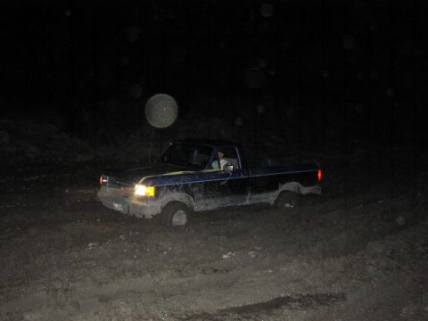 1981 Ford Bronco - Ford F-Series truck stuck in mud at night with headlights on.