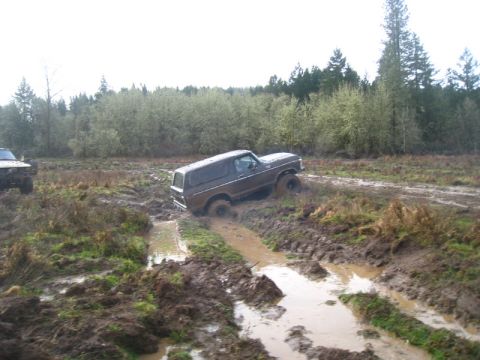 1978 Ford Bronco - A brown 1978 Ford Bronco navigates a muddy off-road course, with another vehicle partially visible on the left.