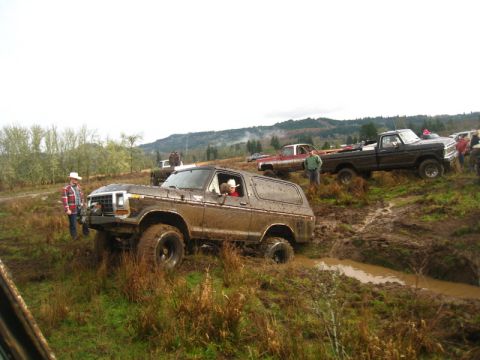 1978 Ford Bronco - Several trucks navigate a muddy off-road course, with a 1978 Ford Bronco prominently featured.