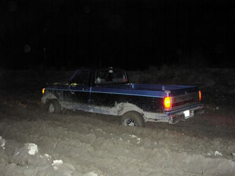 1981 Ford Bronco - This truck is deeply stuck in the mud at night, with its rear lights illuminated.