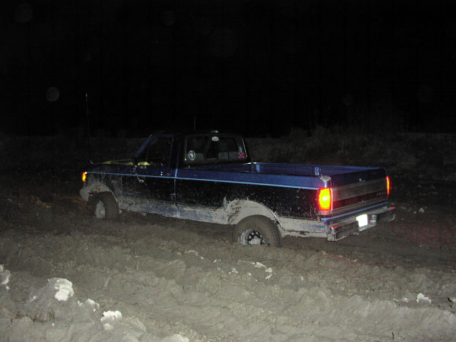 Blue Ford F-Series truck stuck in deep mud at night