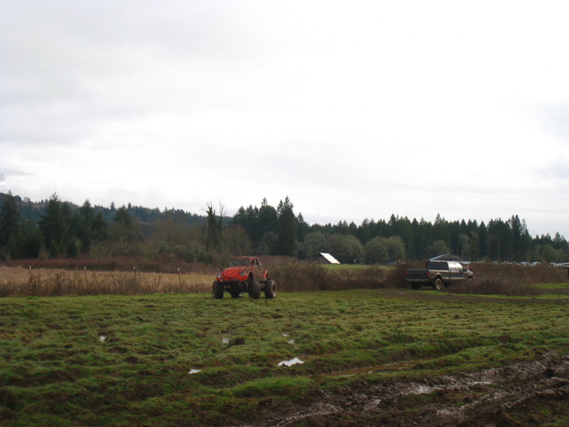 Red off-road buggy and a pickup truck in a muddy field with trees in the background
