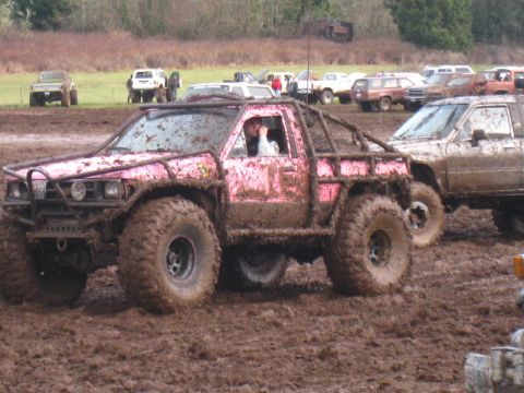1978 Ford Bronco - A pink pickup truck navigates a muddy course with other vehicles in the background.