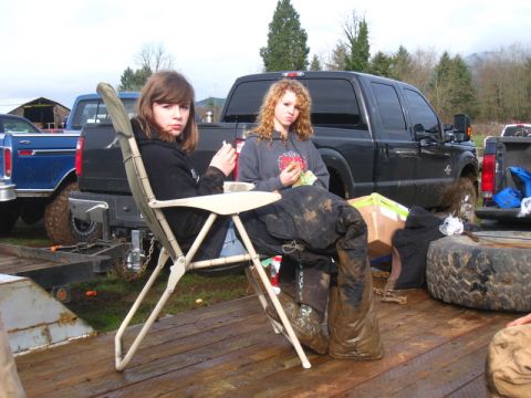 1978 Ford Bronco - Two girls relax on a trailer between mud-covered trucks.