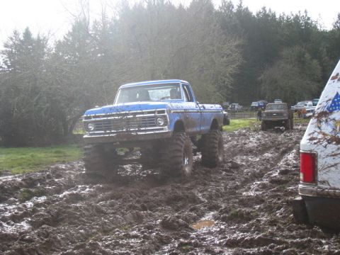 1978 Ford Bronco - This lifted blue pickup truck is navigating a muddy off-road course with other vehicles present.