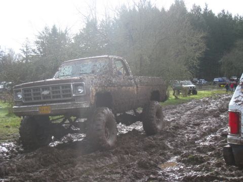 1978 Ford Bronco - A heavily muddied pickup truck navigates a challenging off-road course with other vehicles in the background.