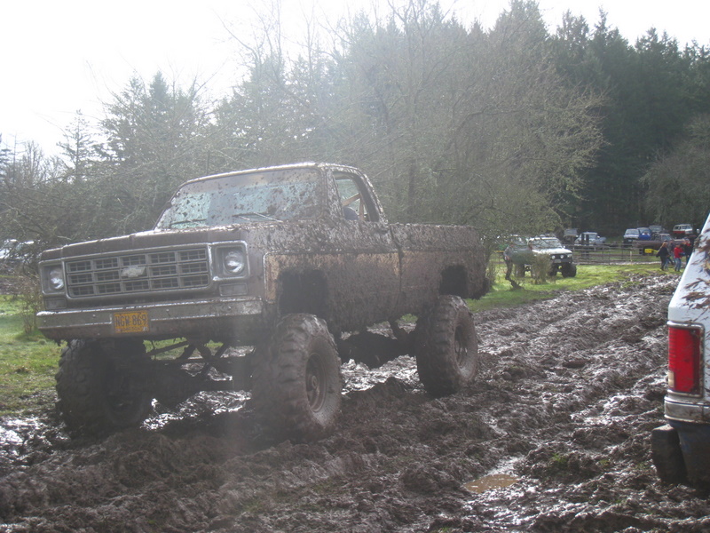 Mud-covered pickup truck with lifted suspension driving through mud