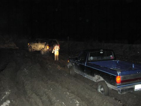 1981 Ford Bronco - Two vehicles are stuck in muddy terrain at night, with one person standing between them.