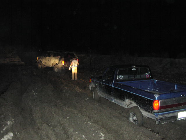 Blue pickup truck and white SUV stuck in mud at night