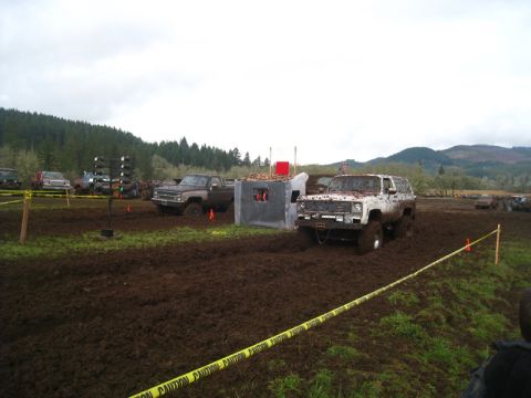 1978 Ford Bronco - A white SUV is stuck in the mud during an off-road event, with other vehicles and a muddy landscape in the background.