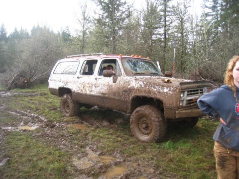 1978 Ford Bronco - Muddy SUV stuck in a field with trees in the background. A person stands nearby.