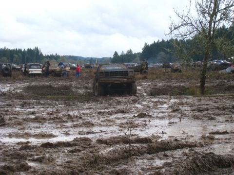 1978 Ford Bronco - Multiple vehicles are bogged down in a muddy field under an overcast sky.
