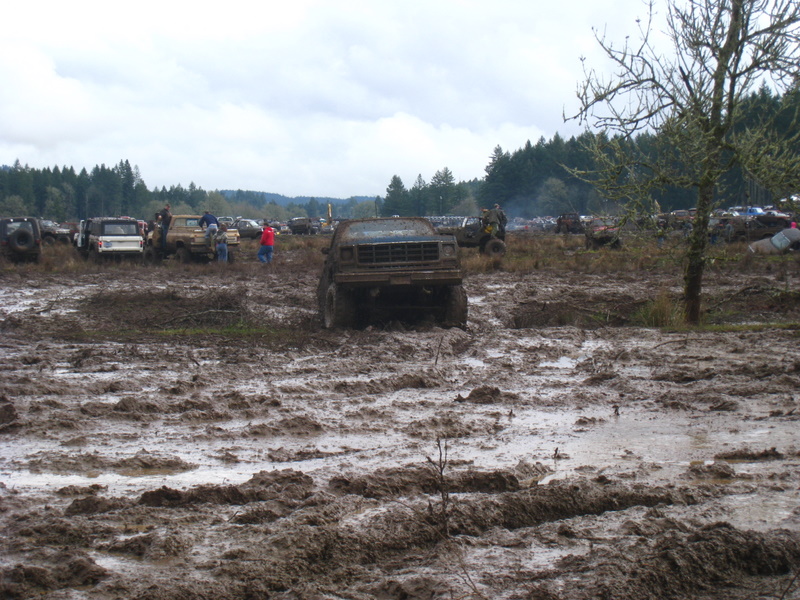 Muddy field with several off-road vehicles stuck in the mud. One truck is in the foreground