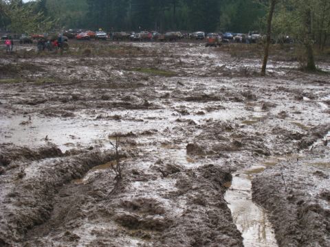 1978 Ford Bronco - A muddy field with numerous off-road vehicles parked in the distance.