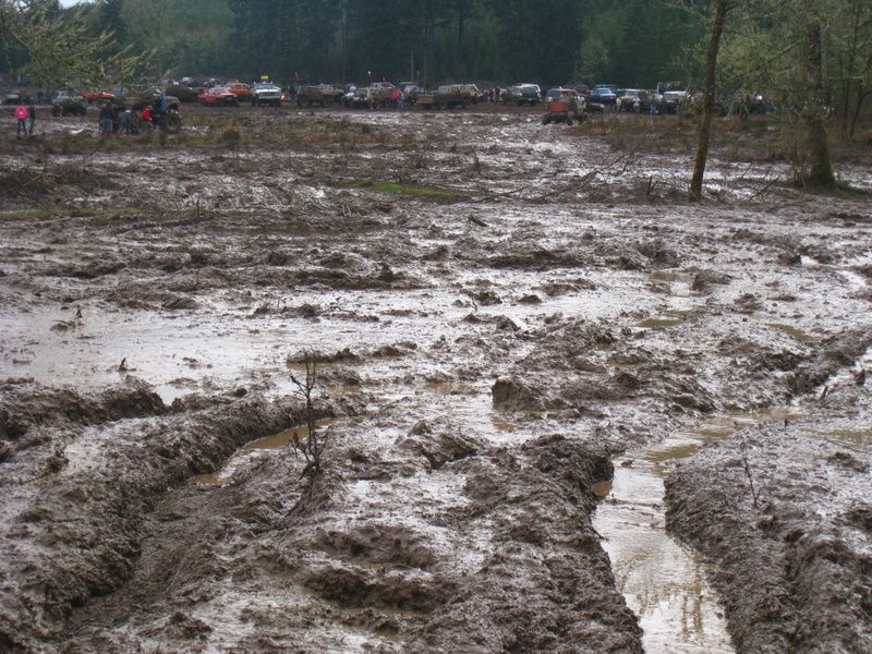 Muddy field with many off-road vehicles in the background