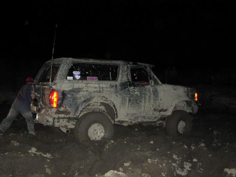 1981 Ford Bronco - A mud-covered 1981 Ford Bronco is stuck in the mud at night, with a person attempting to push it.