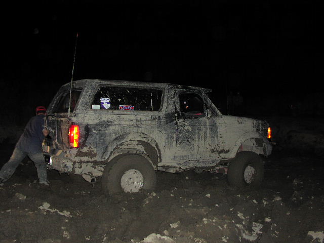 Mud-covered 1981 Ford Bronco stuck in mud at night, rear view
