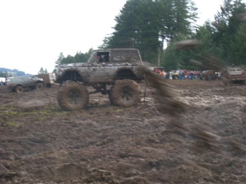 1978 Ford Bronco - A heavily modified off-road vehicle churns up mud during an event, with spectators gathered nearby.