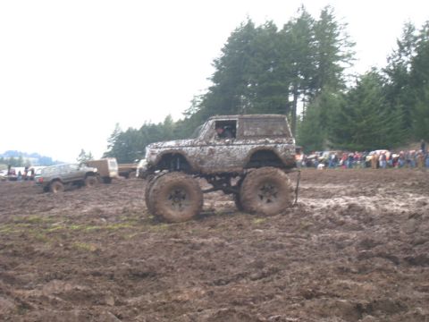 1978 Ford Bronco - A heavily modified 1978 Ford Bronco navigates a muddy off-road course with spectators in the background.