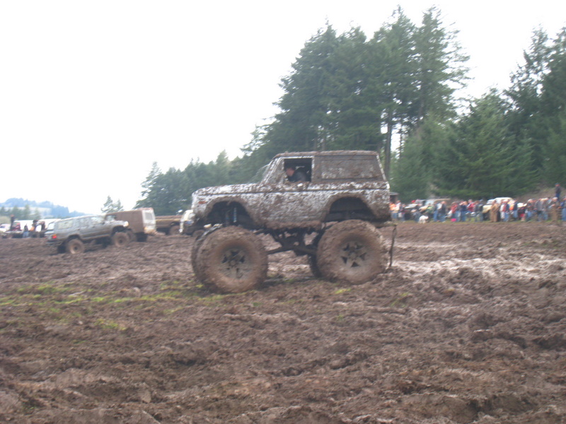 Mud-covered 1978 Ford Bronco with oversized tires in a muddy field