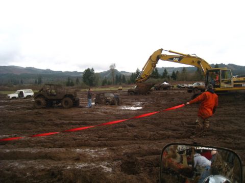 1978 Ford Bronco - Multiple off-road vehicles are stuck in a muddy field, with an excavator nearby and a person holding a red ribbon.