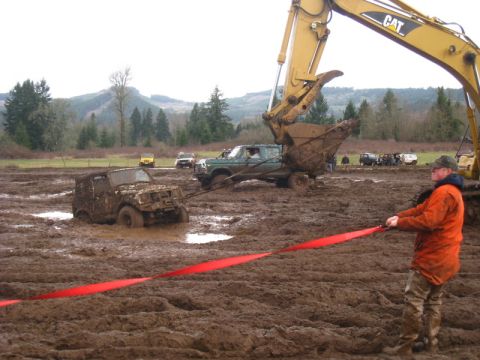1978 Ford Bronco - An excavator is pulling a vehicle out of deep mud while other off-road vehicles are also stuck in the mire.