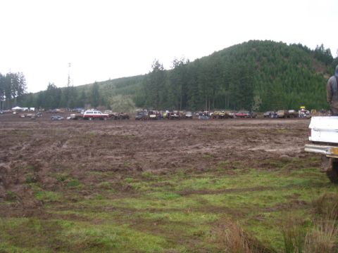 1978 Ford Bronco - A large gathering of vehicles are parked in a muddy field, with a wooded hill in the background.